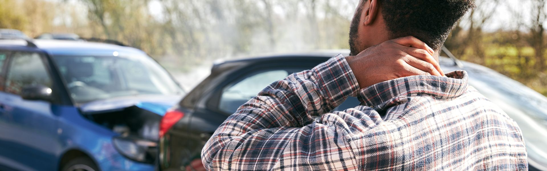 Young man rubbing neck in pain from whiplash injury standing by damaged car after traffic accident