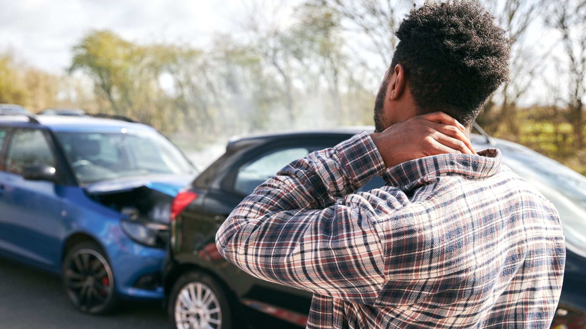 Young man rubbing neck in pain from whiplash injury standing by damaged car after traffic accident